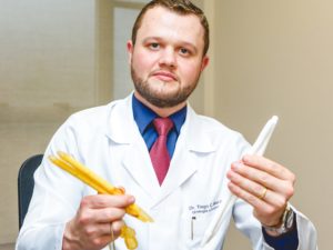 Dr. Tiago Mierzwa de jaleco segurando uma prótese peniana