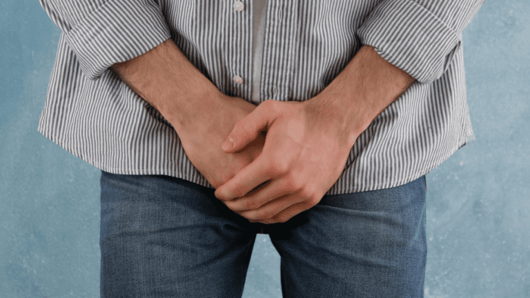 Homem de camisa e calça jeans, com as mãos sobre o pênis, pensando no diagnóstico e tratamento da varicocele