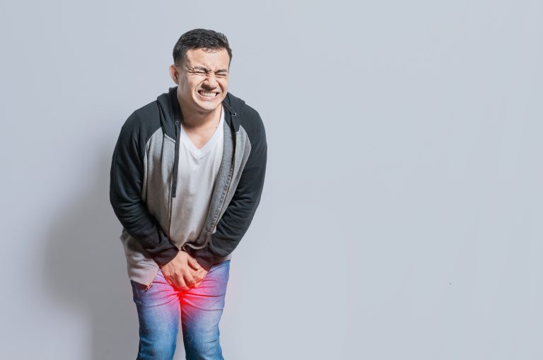 Homem com cara de dor e as mãos sobre a região íntima com Dor no testículo ao final do dia.